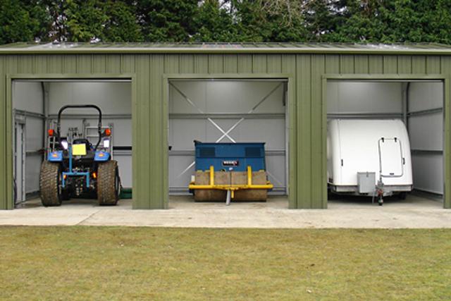 Farm machinery stored inside three open bays of a building
